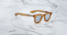 The Jacques Marie Mage Leclair sunglasses, featuring square thick translucent amber frames with silver accents, are displayed on a white marble surface.