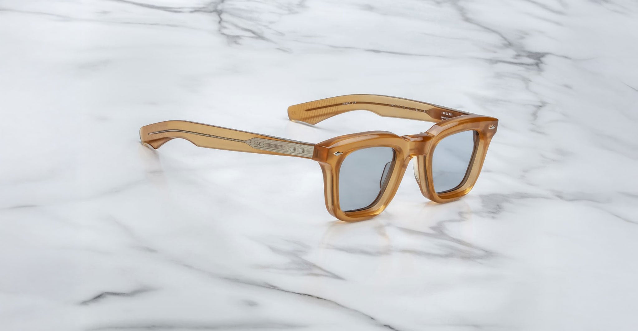 The Jacques Marie Mage Leclair sunglasses, featuring square thick translucent amber frames with silver accents, are displayed on a white marble surface.