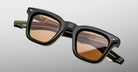 The Jacques Marie Mage Leclair sunglasses feature square-shaped frames in thick dark green and black acetate with brown-tinted lenses, displayed against a light gray background.