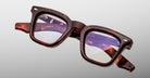 The Jacques Marie Mage Leclair eyeglasses feature thick, square tortoiseshell frames with clear lenses, shown against a plain light gray background. Visible brand markings and details are present on the inner arms.