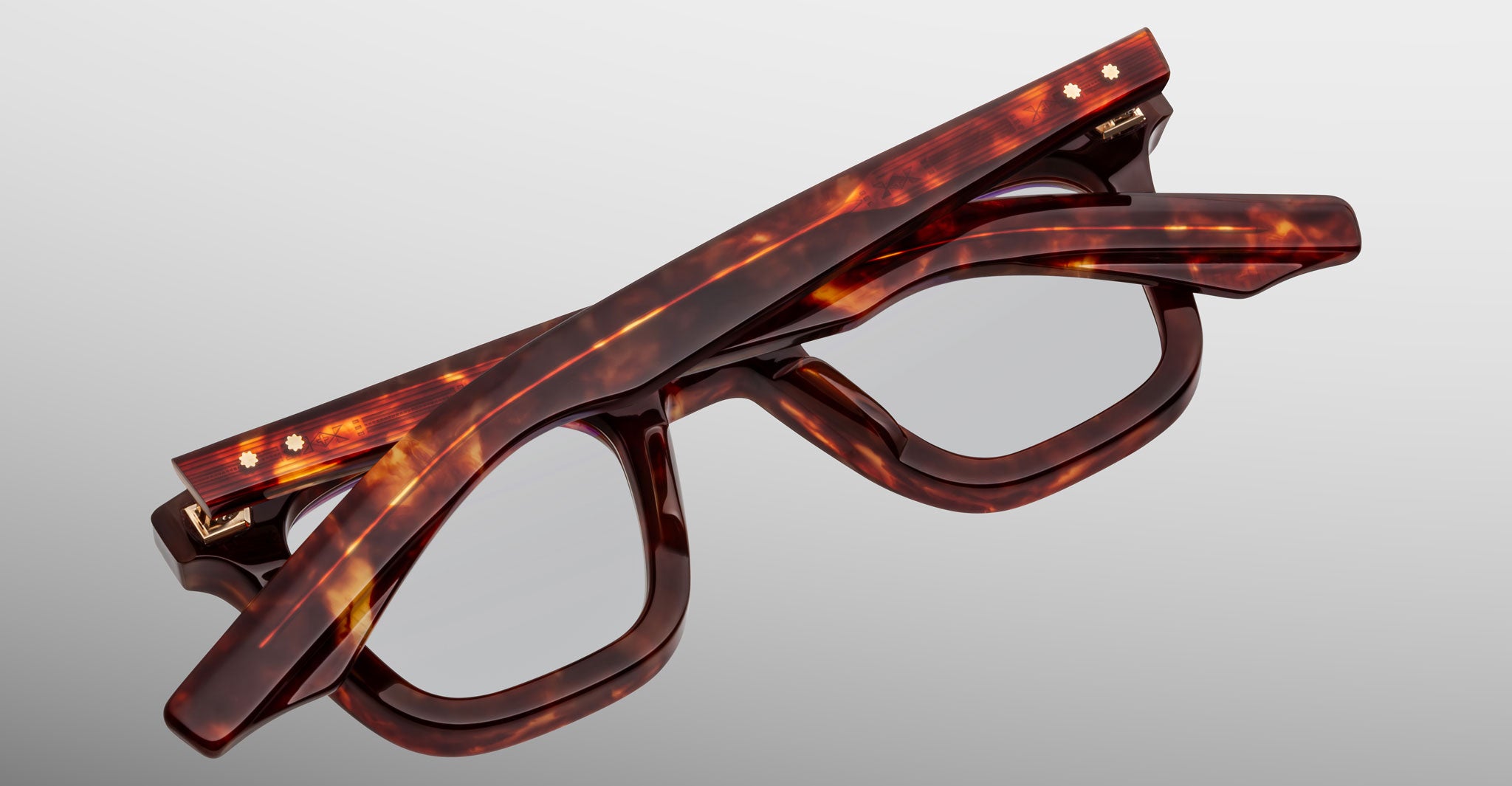 The Jacques Marie Mage Leclair eyeglasses, featuring a tortoiseshell pattern and rectangular lenses, are shown folded on a light gray background.