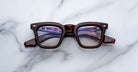 A pair of Jacques Marie Mage Leclair rectangular, thick-framed eyeglasses with a dark tortoiseshell pattern rests on a white marble surface.