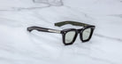 The Jacques Marie Mage Leclair sunglasses feature black rectangular frames with silver temple accents, tinted lenses, and gold text on the inner arms, displayed on a white marble surface.
