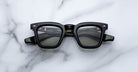 The Jacques Marie Mage Leclair sunglasses, featuring a black rectangular frame with subtle patterned temples and metallic accents near the hinges, rest on a white marble surface. The lenses are dark for a sleek, modern look.