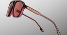 The Jacques Marie Mage Leonard sunglasses feature thick, rectangular dark red frames with matching red-tinted lenses, gold-accented temples, and are shown angled against a plain gray background.