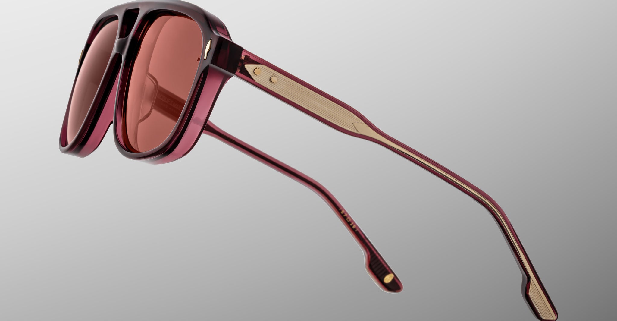 The Jacques Marie Mage Leonard sunglasses feature thick, rectangular dark red frames with matching red-tinted lenses, gold-accented temples, and are shown angled against a plain gray background.