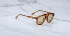 Jacques Marie Mage Leonard sunglasses featuring tortoiseshell-patterned thick frames and brown-tinted lenses are displayed on a white marble surface.