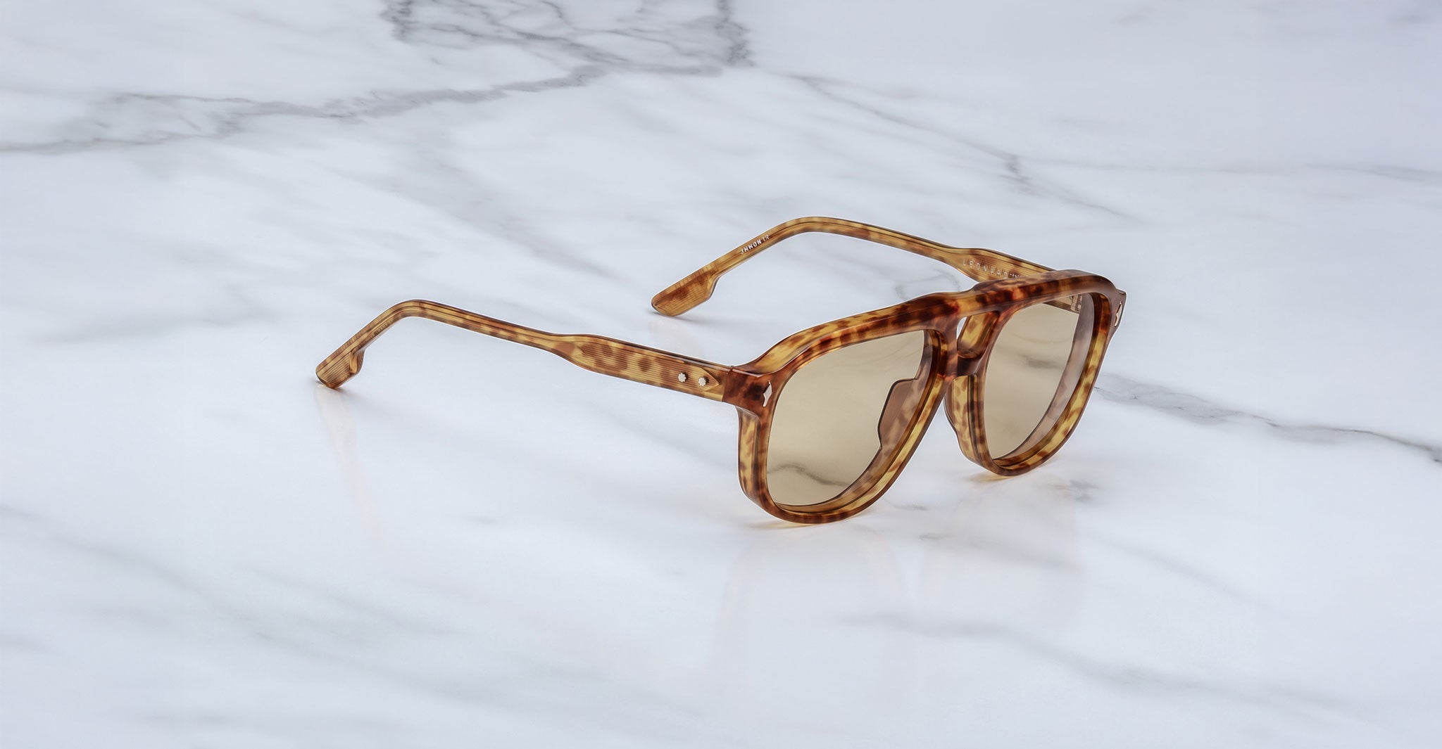 Jacques Marie Mage Leonard sunglasses featuring tortoiseshell-patterned thick frames and brown-tinted lenses are displayed on a white marble surface.