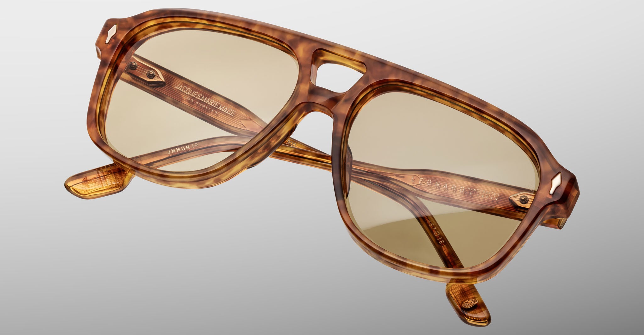 The Jacques Marie Mage Leonard eyeglasses feature brown tortoiseshell aviator-style frames with a double bridge and light yellow-tinted lenses, plus visible branding on the inner arms, shown against a plain gray background.