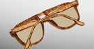 The Jacques Marie Mage Leonard, brown tortoiseshell sunglasses with beige lenses, are displayed upside down on a light gray background, their arms crossed over each other.