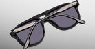 A close-up of Jacques Marie Mage Leonard sunglasses, showcasing black frames with dark lenses and metallic temple accents, set against a light grey background.