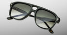 Close-up of Jacques Marie Mage Leonard black square-framed sunglasses with dark gradient lenses and subtle metallic accents on the arms, shown against a light gray background.