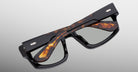 Jacques Marie Mage Louisville eyeglasses in black and tortoiseshell, folded with crossed temples, top-down view.