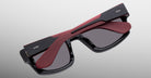 Jacques Marie Mage Louisville sunglasses, black and red with polarized lenses, shown from above on a reflective gray surface.
