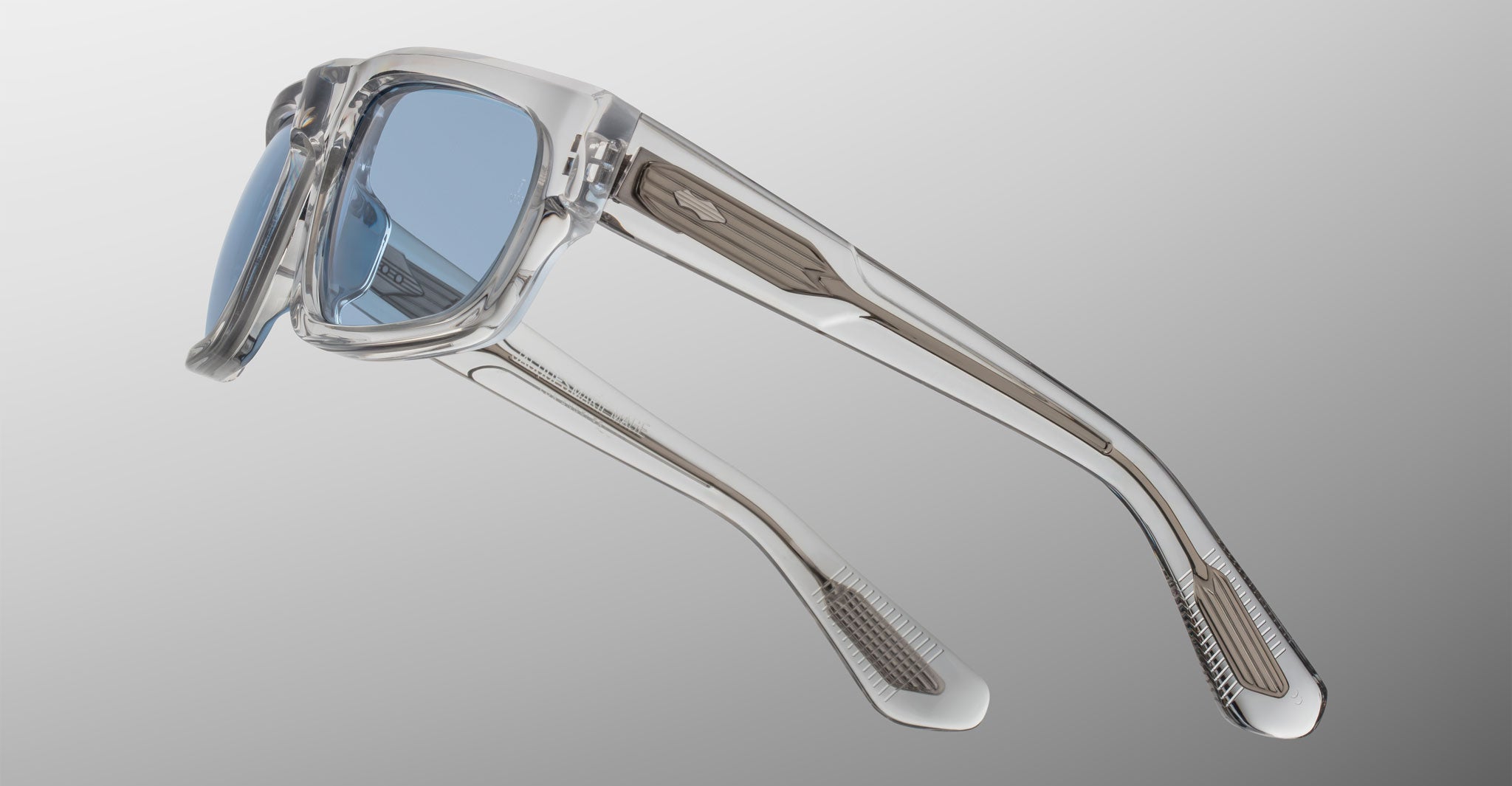 Jacques Marie Mage Louisville sunglasses with clear acrylic frames, blue-tinted lenses, and bold arms shown from a side angle.