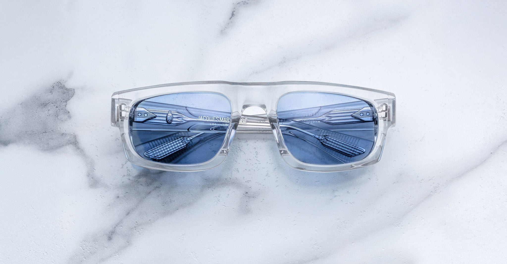 Jacques Marie Mage Louisville sunglasses with clear frames and blue lenses, metallic accents visible, shown from a front angle.