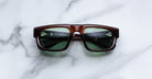 Jacques Marie Mage Louisville sunglasses with brown frames and green lenses, top view, product displayed on a flat surface.