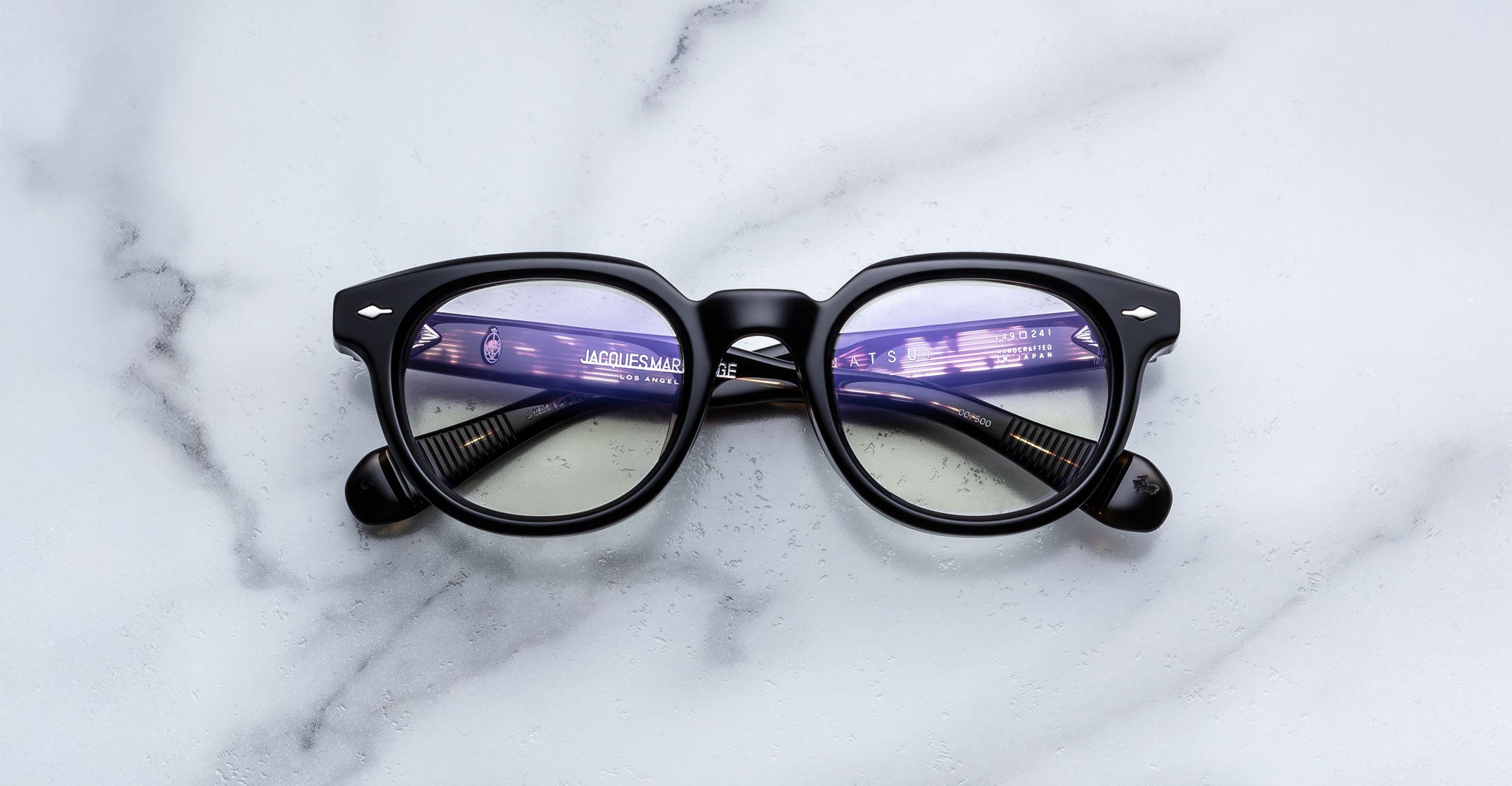 Jacques Marie Mage Matsu eyeglasses with round black frames, purple lens reflection, shown from above.