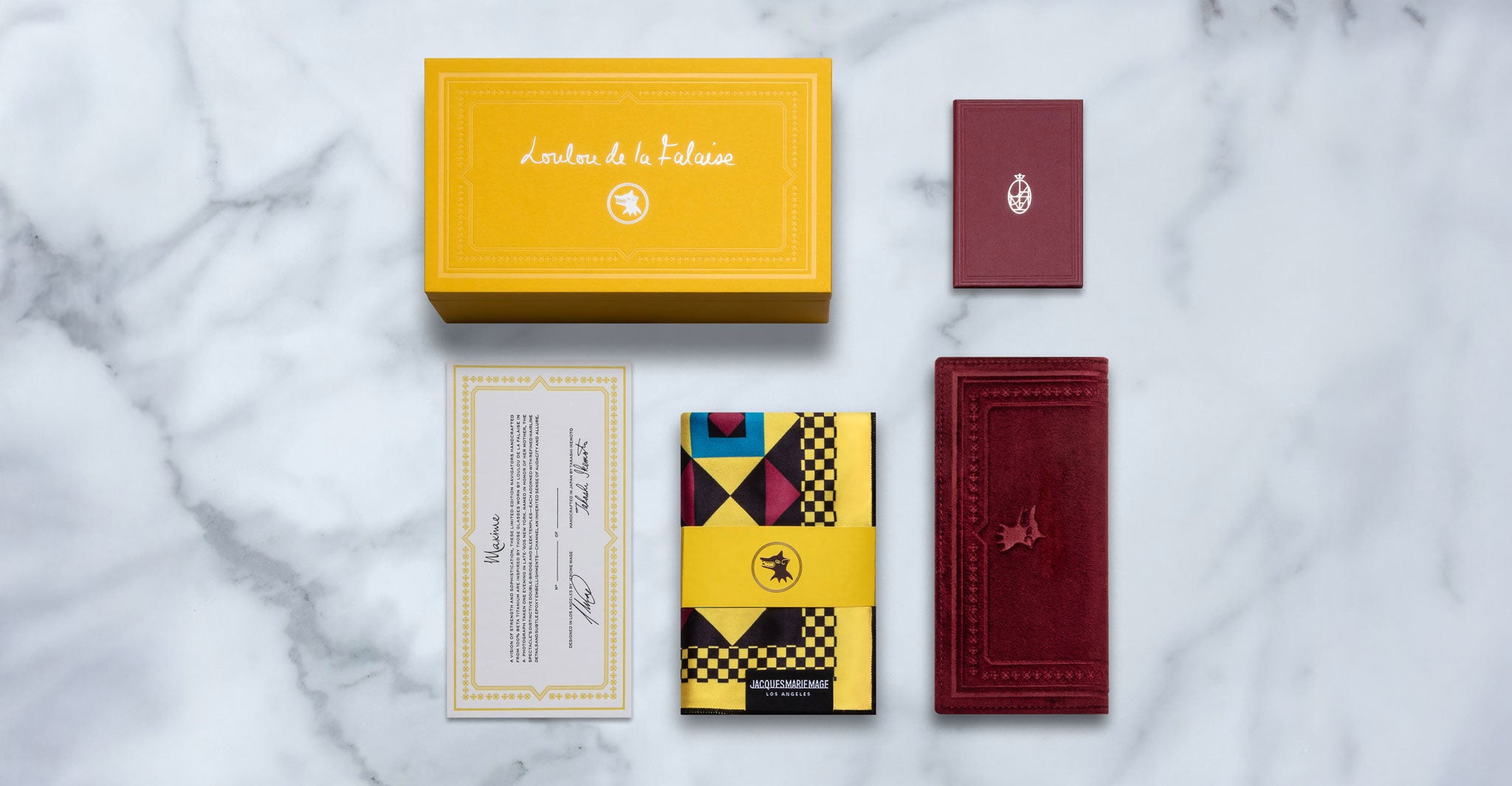 Jacques Marie Mage Maxime eyeglasses packaging with yellow box, maroon wallet, scarf, certificate, and booklet shown top view.