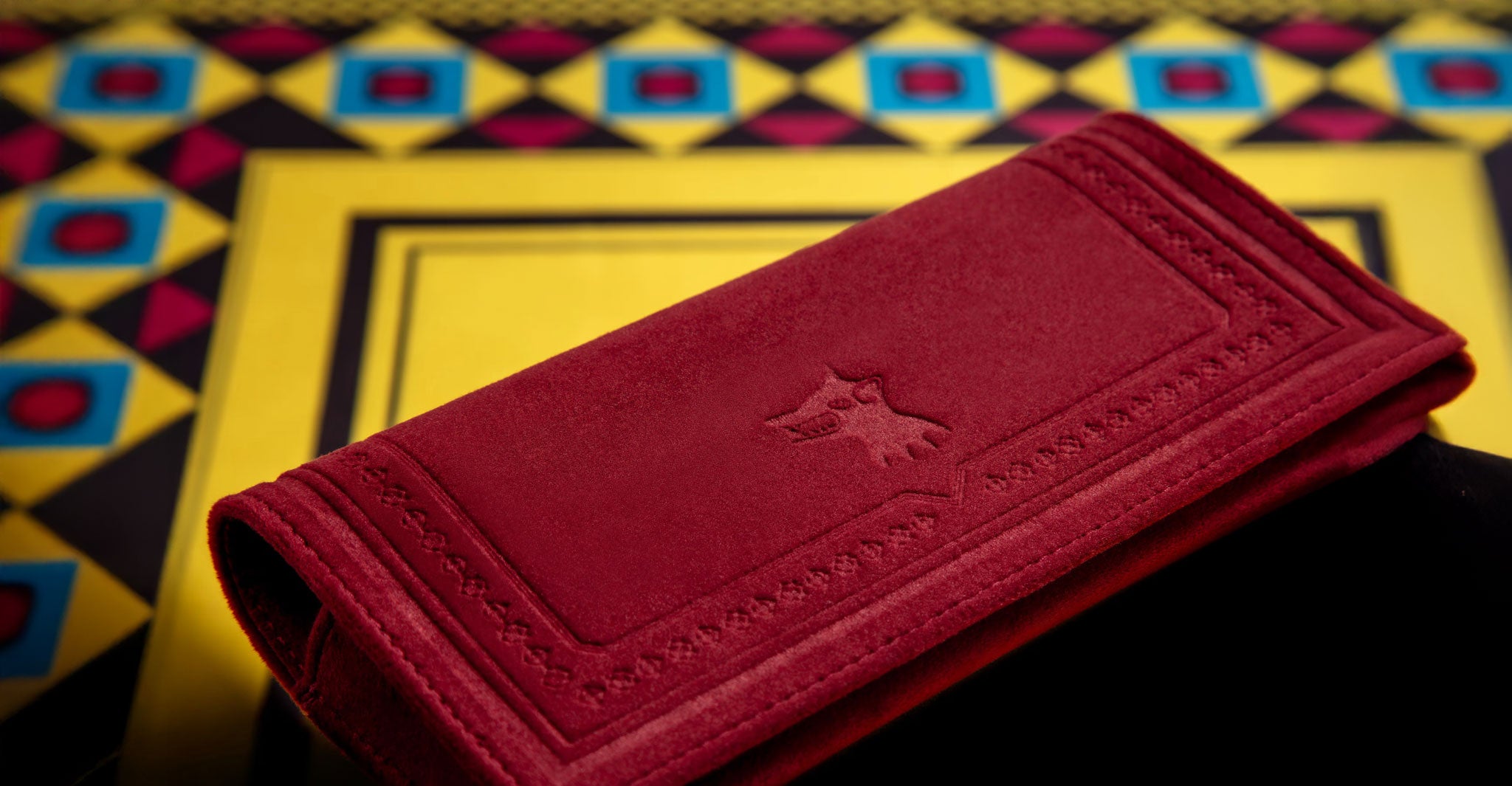 Jacques Marie Mage Maxime wallet in red suede with embossed animal logo on geometric surface, shown from front angle.