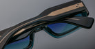 A close-up of two pairs of Jacques Marie Mage Miglia sunglasses with dark frames and blue-tinted lenses, stacked together, highlighting their metallic accents and detailed arms.