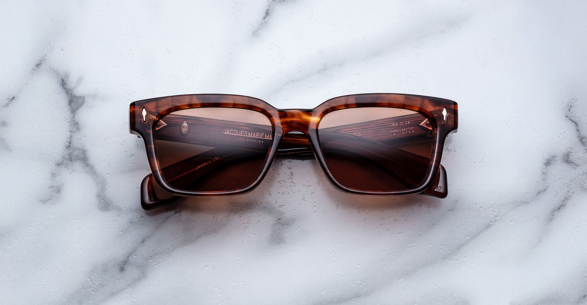 A pair of Jacques Marie Mage Molino 55 brown tortoiseshell square sunglasses with dark lenses rests on a white marble surface.