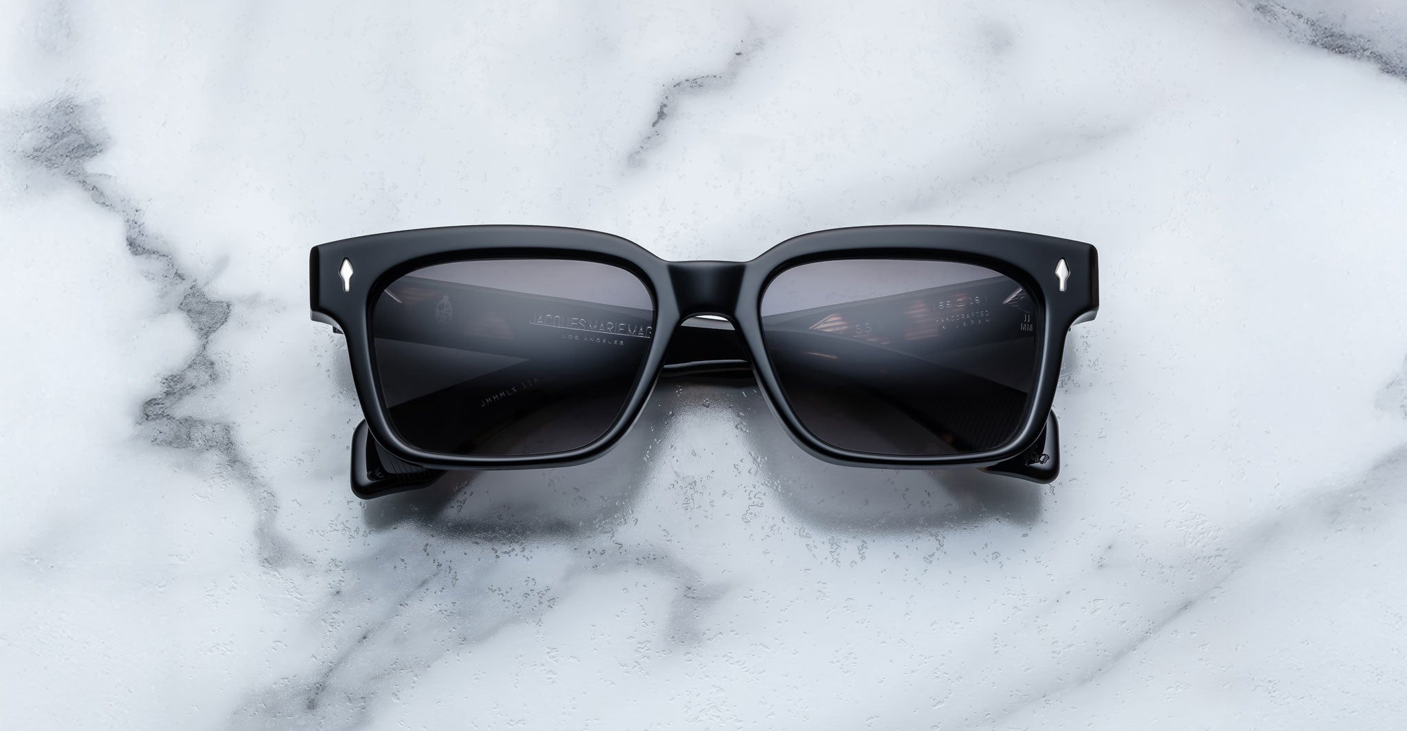 A pair of Jacques Marie Mage Molino 55 black rectangular sunglasses with dark lenses is placed on a white marble surface.