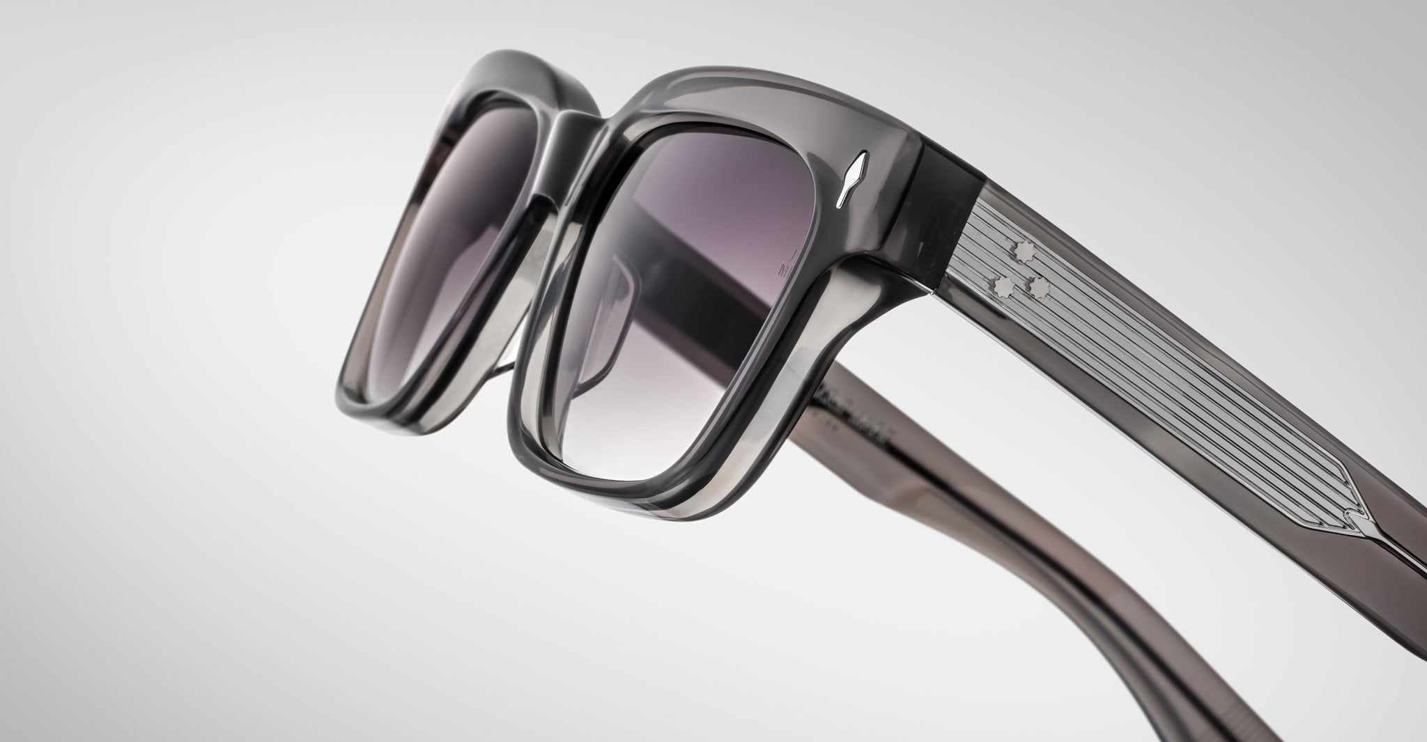 Close-up of Jacques Marie Mage Molino 55 sunglasses featuring stylish thick black frames, slightly tinted lenses, and metallic detailing on the arms against a light gray background.