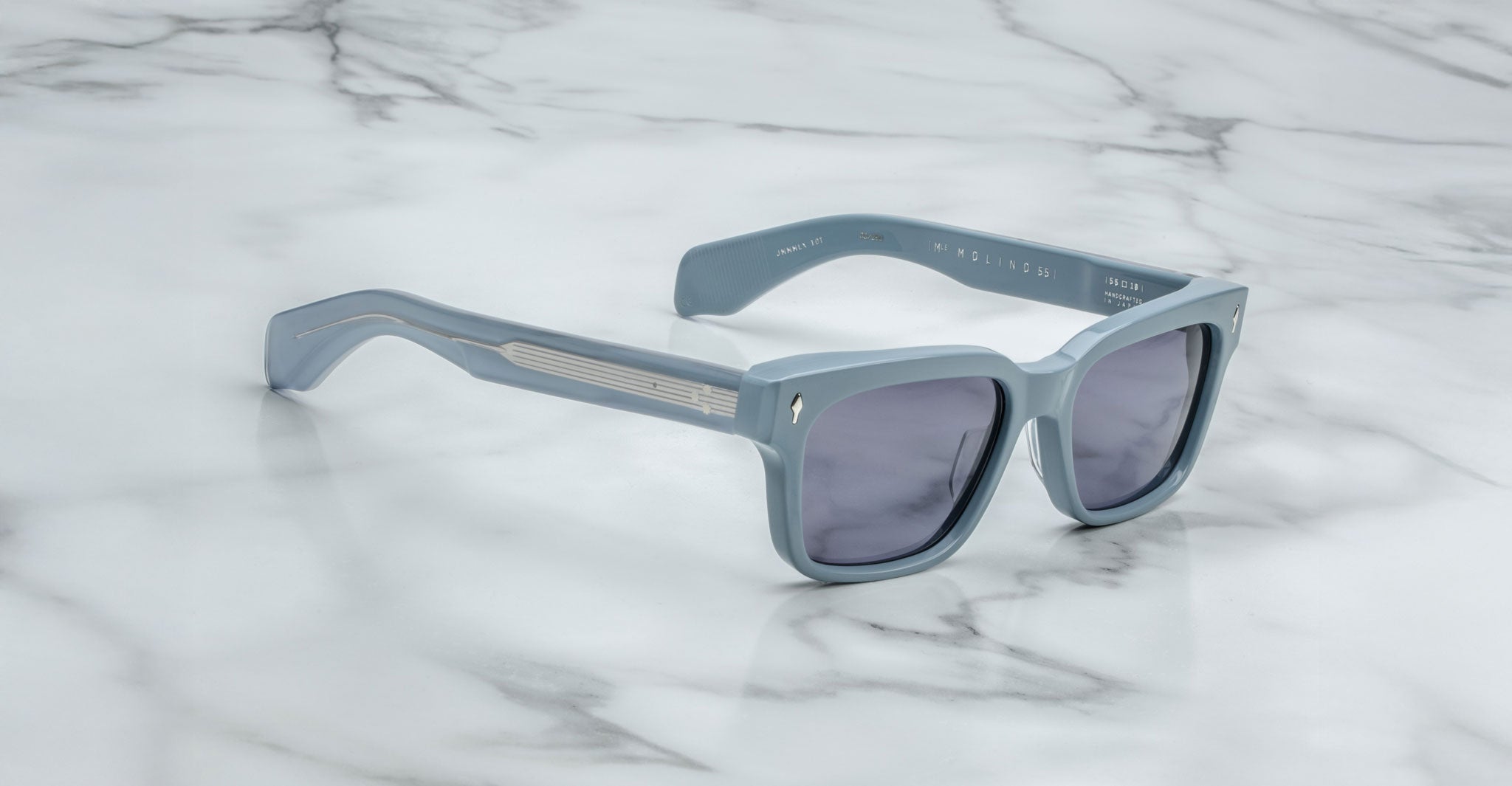 The Jacques Marie Mage Molino 55: light blue square sunglasses with dark lenses and thick frames are displayed on a white marble surface.