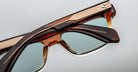 Close-up of two Jacques Marie Mage Molino eyeglasses, brown and gold frames, blue lenses, front view.