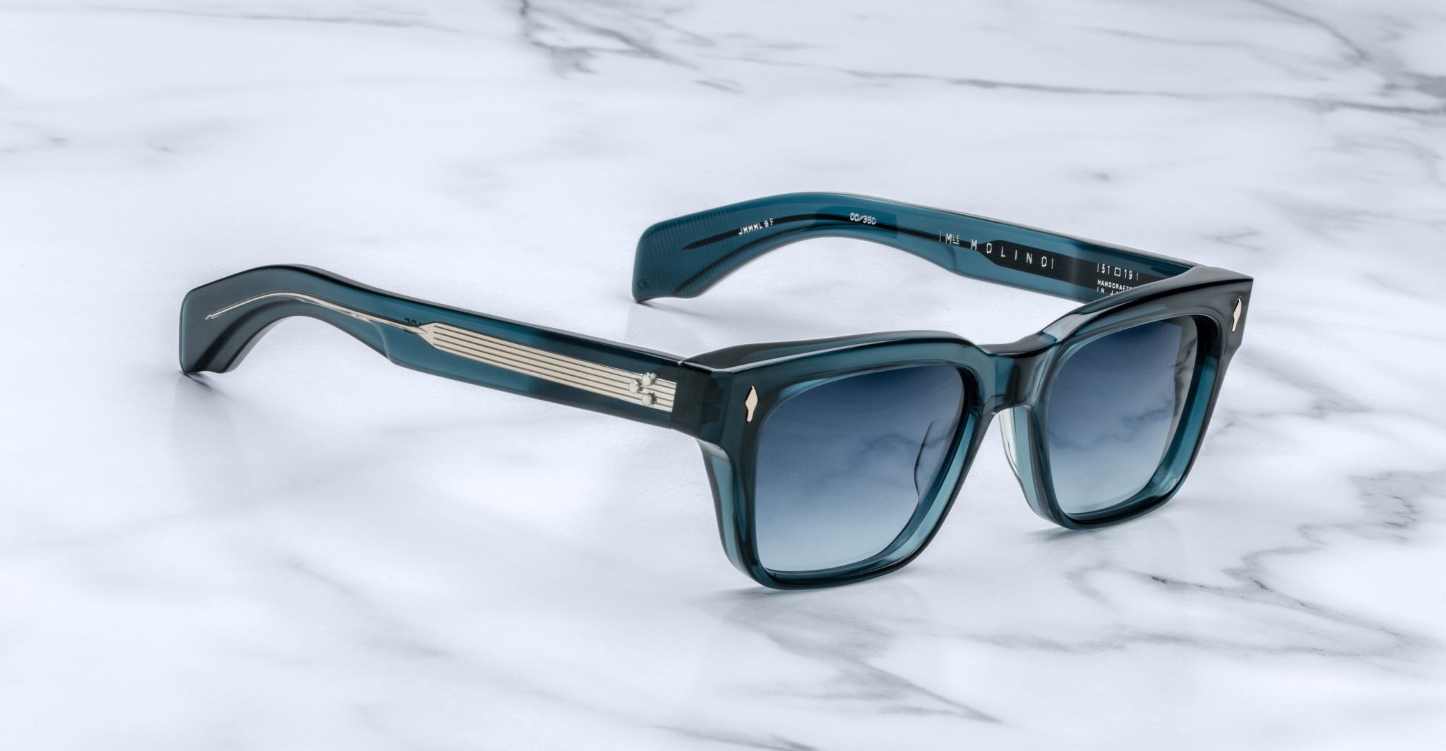 Jacques Marie Mage Molino sunglasses in teal with dark gradient lenses and metallic accents, shown from above.