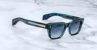 Jacques Marie Mage Molino sunglasses in teal with dark gradient lenses and metallic accents, shown from above.