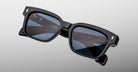 Jacques Marie Mage Molino sunglasses are black, rectangular with dark lenses and thick frames, displayed on a light gray background. Brand details in white text appear inside the arm.