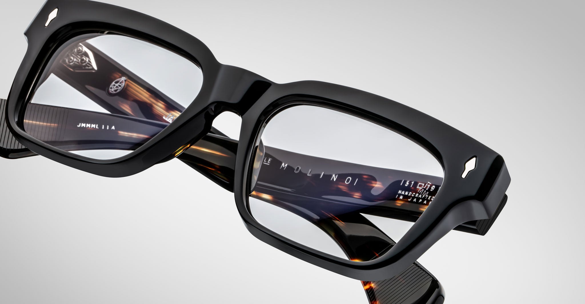 Close-up of Jacques Marie Mage Molino eyeglasses by Jacques Marie Mage, featuring thick black frames and tortoiseshell-patterned arms with brand markings visible inside the temples, set against a plain light background.