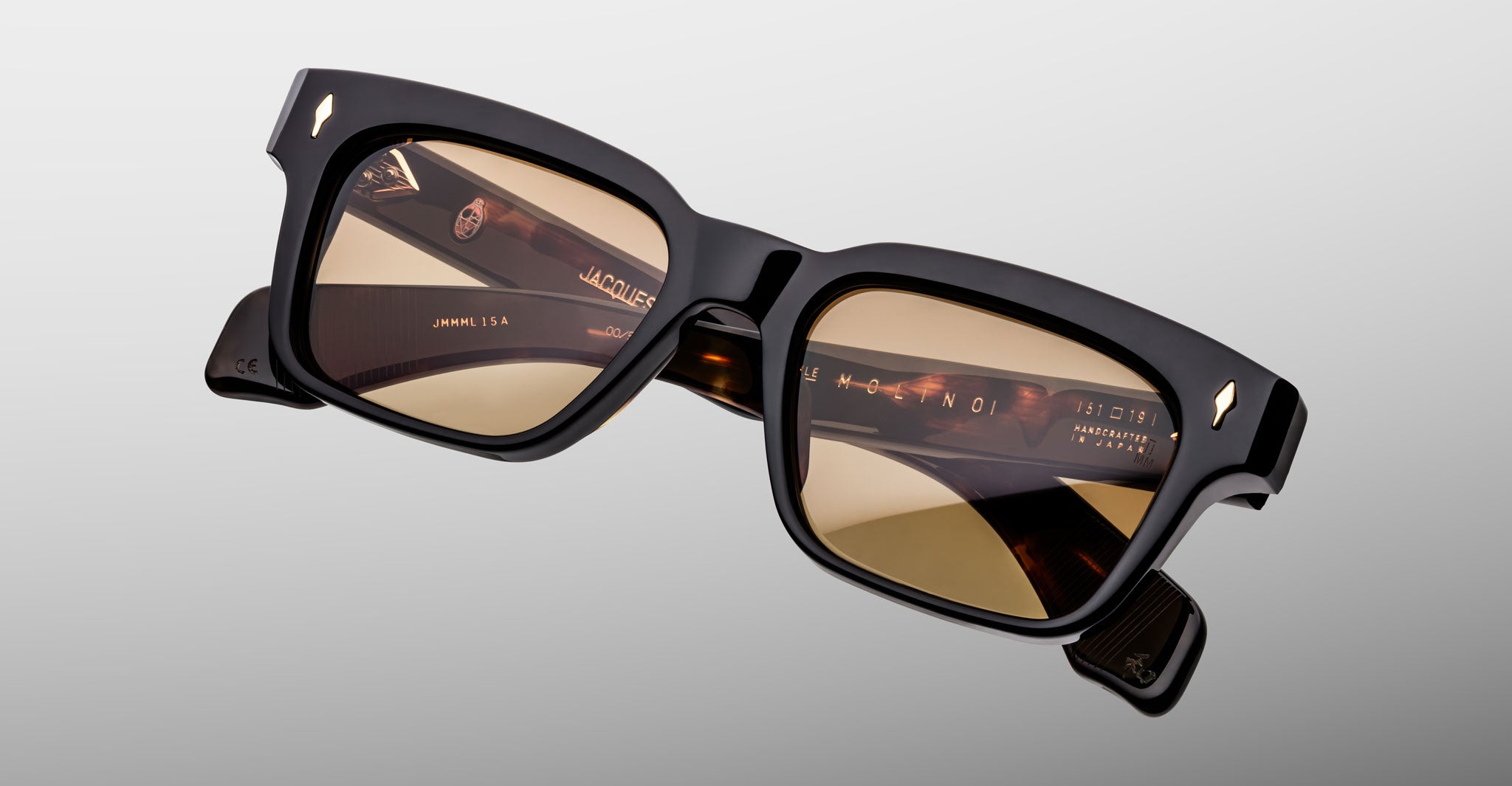 The Jacques Marie Mage Molino by COMING SOON: stylish, chunky black sunglasses with rectangular brown-tinted lenses shown on a light gray background.