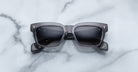 Jacques Marie Mage Molino rectangular gray sunglasses by COMING SOON, featuring dark tinted lenses, rest on a white marble surface.