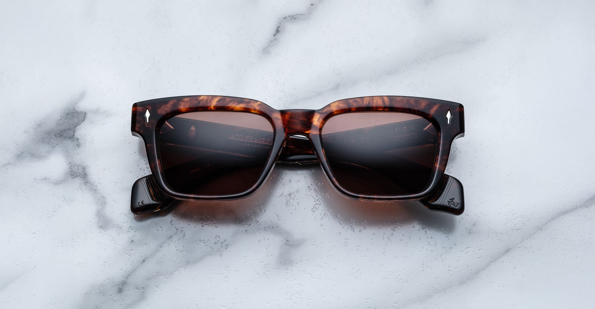Jacques Marie Mage Molino sunglasses by COMING SOON, featuring square tortoiseshell frames and dark lenses, displayed on a white marble surface with subtle grey veining.