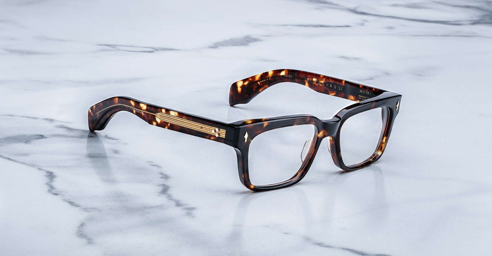 The Jacques Marie Mage Molino 55 tortoiseshell rectangular eyeglasses with thick frames rest on a white marble surface with grey veins.