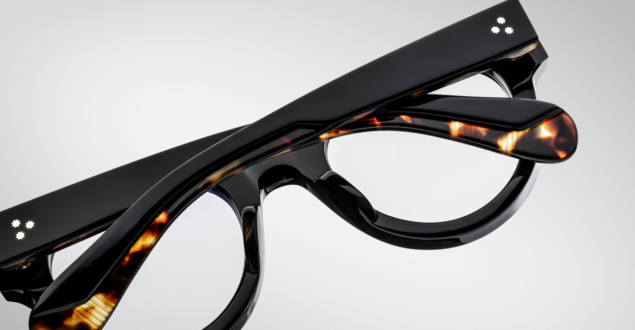 A close-up of folded Jacques Marie Mage Molitor eyeglasses with black and tortoiseshell-patterned frames, resting on a light gray background.