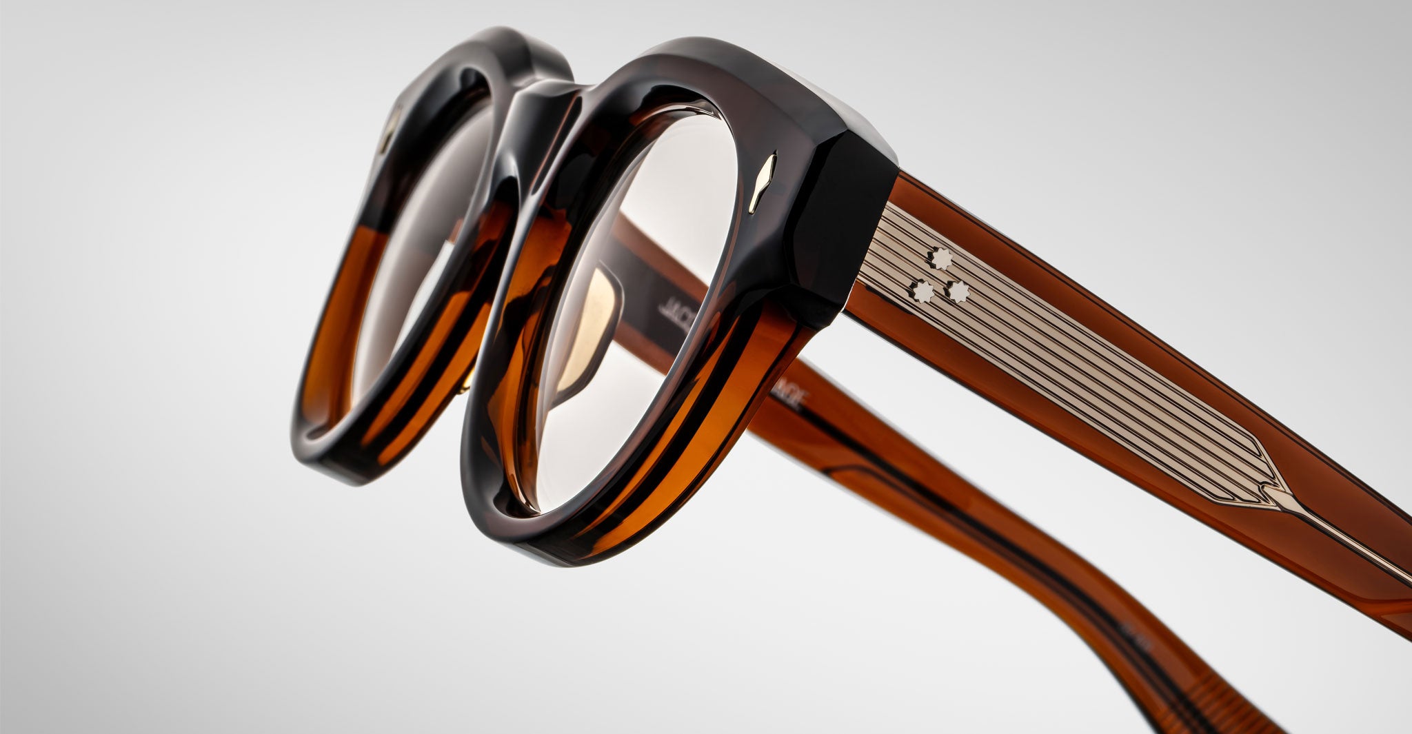 Close-up of Jacques Marie Mage Molitor eyeglasses—thick, brown, rectangular frames with wide arms, metal temple detailing, and clear lenses—set against a plain light gray background.