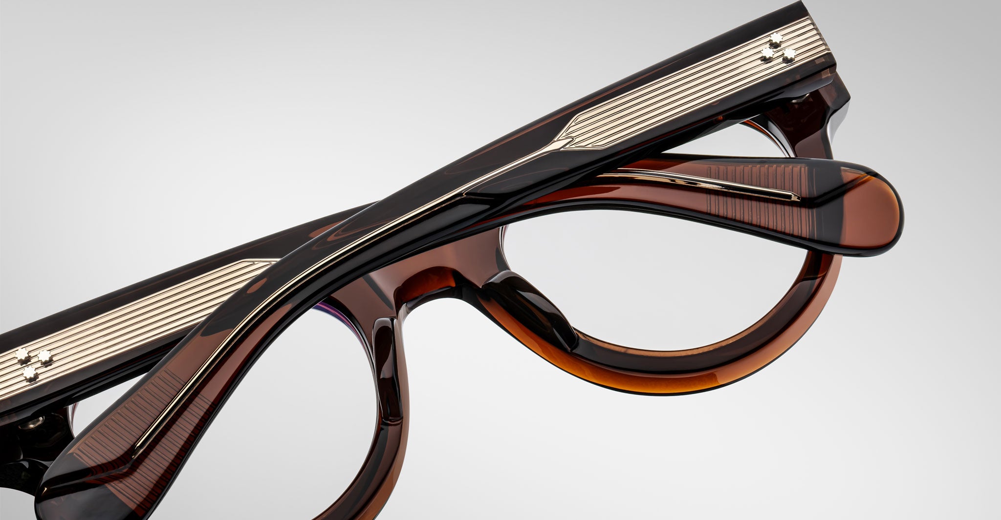 A close-up of the Jacques Marie Mage Molitor eyeglasses in brown and black with silver detailing on the temples, shown folded on a plain light background.