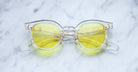The Jacques Marie Mage Mont Blanc eyeglasses, featuring clear frames and round yellow-tinted lenses, are displayed on a white marble surface.