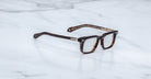 Jacques Marie Mage Moscova in Beau acetate optical frame, angled view with rectangular lenses, rich tortoiseshell acetate front, signature arrowhead pins, and exposed core wire temples with warm tonal detailing