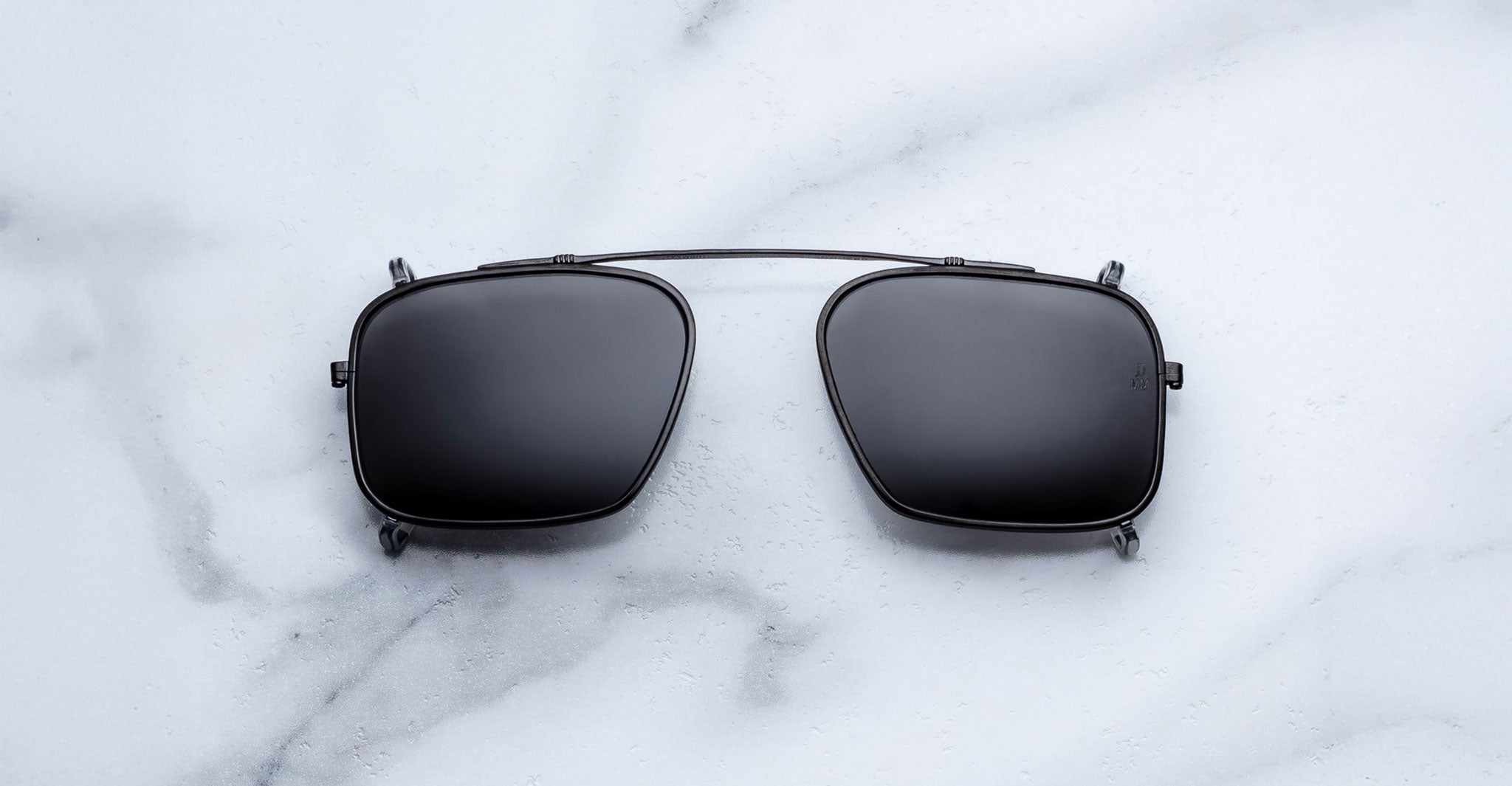 Jacques Marie Mage Moscova clip-on in Black, front-facing view with rectangular dark-tinted lenses, slim black metal frame, and bridge-mounted clip mechanism designed to attach seamlessly to Moscova optical frames
