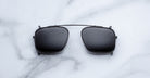 Jacques Marie Mage Moscova clip-on in Black, front-facing view with rectangular dark-tinted lenses, slim black metal frame, and bridge-mounted clip mechanism designed to attach seamlessly to Moscova optical frames