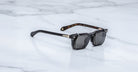 Jacques Marie Mage Moscova in Noir 15 acetate optical frame with Black clip-on, angled view featuring rectangular dark-tinted lenses, polished black acetate, signature arrowhead pins, and slim black clip-on attachment with exposed core wire temples