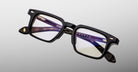 Jacques Marie Mage Moscova in Noir 15 acetate optical frame, angled view highlighting rectangular lenses, bold sculpted black front, signature arrowhead pins, and exposed core wire temples with warm tortoiseshell interior detailing