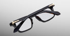 Jacques Marie Mage Moscova in Noir 15 acetate optical frame, top-down angled view showcasing bold rectangular silhouette, polished black acetate, arrowhead front pins, and gold monoblock hinges with sculpted temples