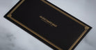 Jacques Marie Mage Kinshasa eyeglasses on a black card with gold border, centered gold text, front view.