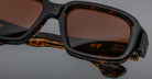 Close-up of Jacques Marie Mage Nakahira tortoiseshell sunglasses with brown lenses. The inner arm displays gold Japanese characters and HANDCRAFTED IN JAPAN on a plain gray background.